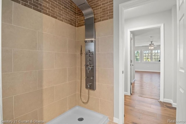 bathroom with ceiling fan, wood-type flooring, tiled shower, and brick wall