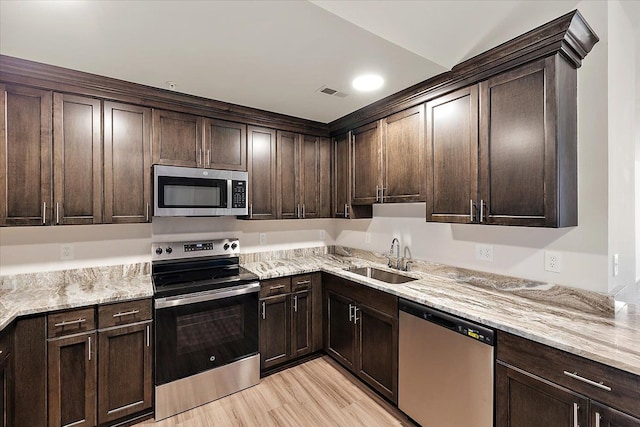 kitchen with light stone countertops, appliances with stainless steel finishes, dark brown cabinetry, and sink