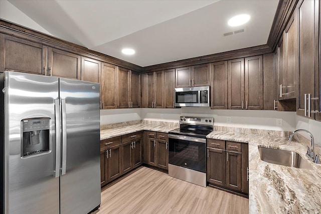 kitchen with light stone countertops, sink, stainless steel appliances, lofted ceiling, and dark brown cabinets