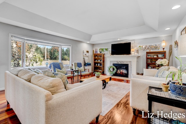 living room with a tray ceiling, a premium fireplace, and hardwood / wood-style flooring