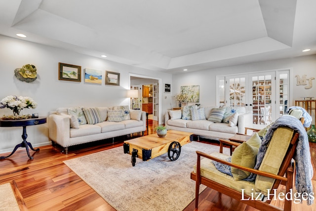 living room with a raised ceiling, hardwood / wood-style floors, and french doors