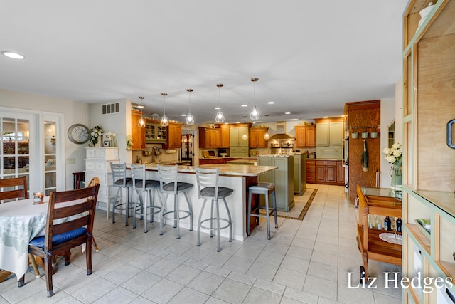 kitchen featuring a kitchen bar, kitchen peninsula, wall chimney exhaust hood, light tile patterned floors, and decorative light fixtures