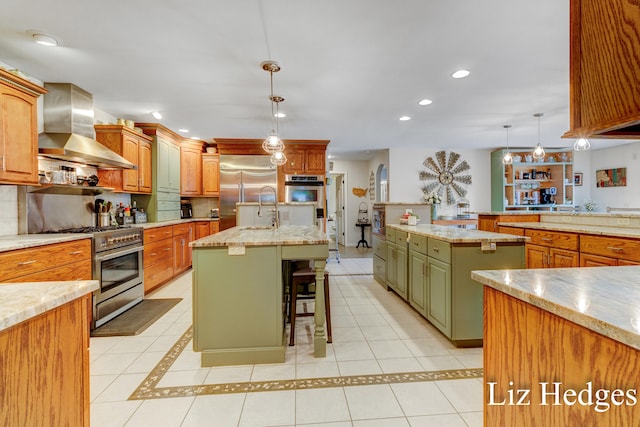 kitchen with a breakfast bar, high quality appliances, a kitchen island with sink, wall chimney range hood, and hanging light fixtures