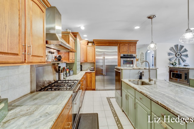 kitchen with sink, hanging light fixtures, wall chimney range hood, tasteful backsplash, and built in appliances