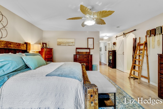 bedroom with a barn door, ceiling fan, and light wood-type flooring