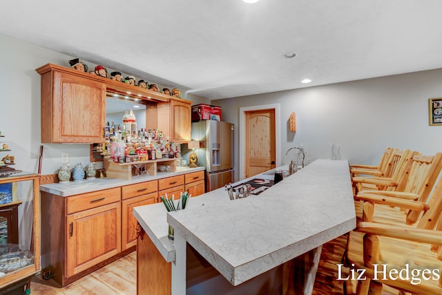 kitchen featuring a breakfast bar, a center island, sink, stainless steel fridge, and light wood-type flooring