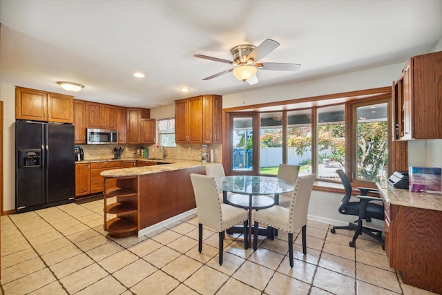 kitchen with kitchen peninsula, backsplash, black fridge, ceiling fan, and sink