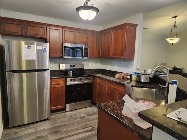 kitchen featuring sink, hanging light fixtures, dark stone countertops, light wood-type flooring, and stainless steel appliances