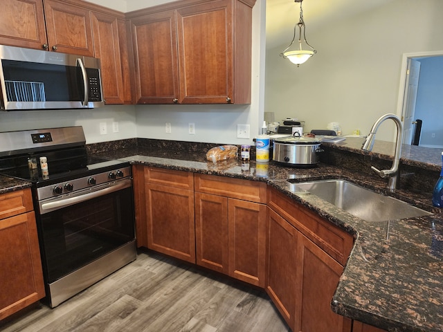 kitchen with sink, stainless steel appliances, dark stone counters, decorative light fixtures, and light wood-type flooring