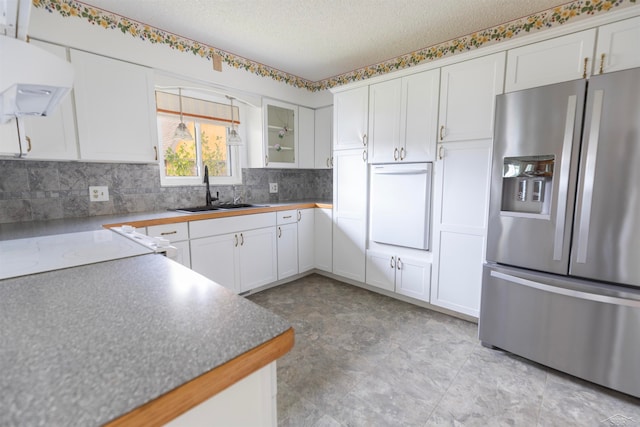 kitchen with stainless steel fridge, a textured ceiling, ventilation hood, sink, and white cabinets