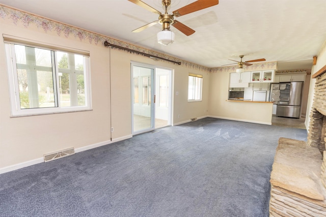 unfurnished living room with dark carpet, ceiling fan, and a stone fireplace