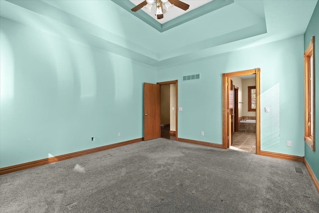 unfurnished bedroom with ceiling fan, a raised ceiling, carpet floors, and connected bathroom