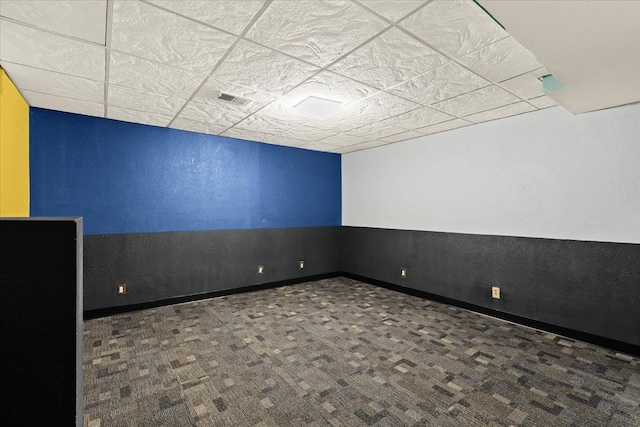 unfurnished room with a paneled ceiling and dark colored carpet