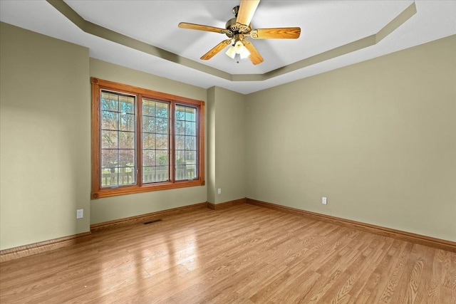 spare room with ceiling fan, a tray ceiling, and light hardwood / wood-style flooring