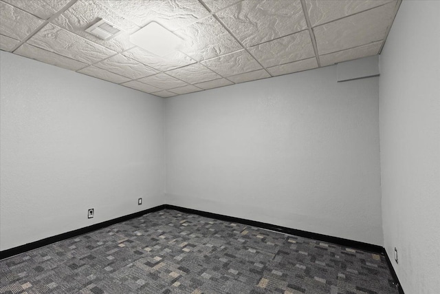 empty room with a paneled ceiling and dark colored carpet