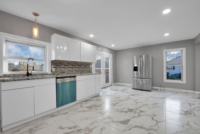 kitchen with white cabinets, light stone counters, stainless steel appliances, and a wealth of natural light