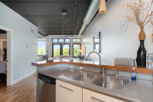 kitchen with kitchen peninsula, sink, stainless steel dishwasher, hardwood / wood-style flooring, and white cabinetry