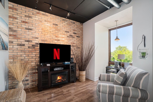 living room featuring wood-type flooring, brick wall, and track lighting