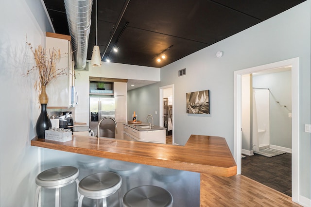 kitchen with track lighting, white cabinets, stainless steel refrigerator with ice dispenser, light hardwood / wood-style flooring, and kitchen peninsula