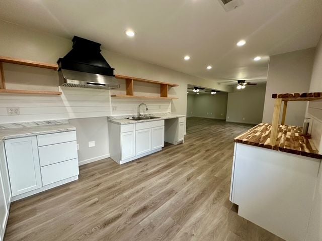 kitchen with sink, wall chimney exhaust hood, ceiling fan, light wood-type flooring, and white cabinetry