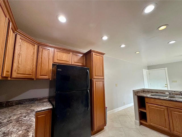 kitchen with black refrigerator, light tile patterned floors, dark stone countertops, and sink