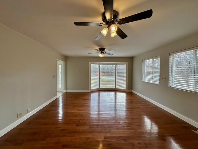 empty room with dark wood-type flooring, ceiling fan, and a healthy amount of sunlight