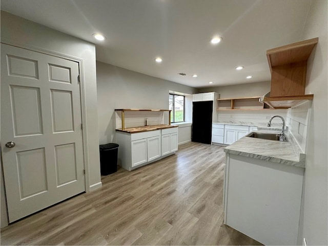 kitchen featuring light stone countertops, light hardwood / wood-style floors, white cabinetry, and sink