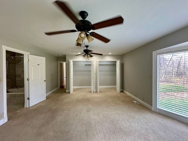 unfurnished bedroom featuring ceiling fan, light carpet, and two closets