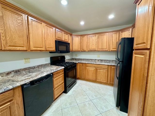 kitchen with light stone countertops, light tile patterned floors, and black appliances