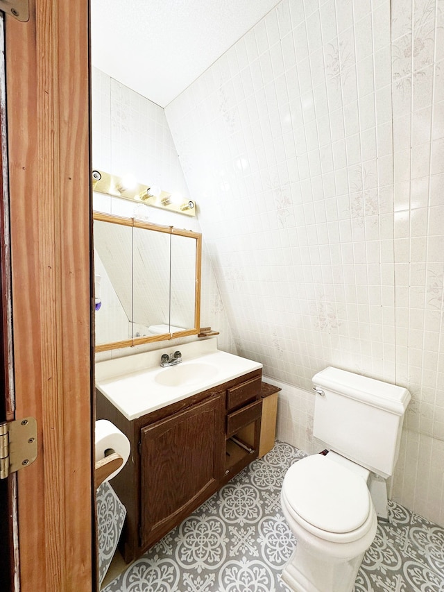 bathroom featuring vanity, toilet, lofted ceiling, and tile walls