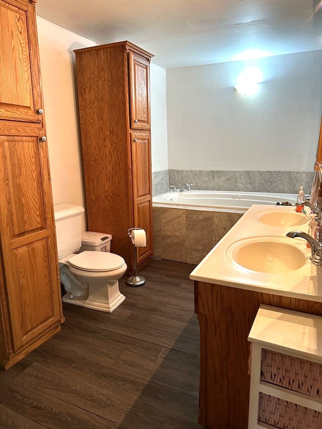 bathroom featuring tiled bath, vanity, wood-type flooring, and toilet