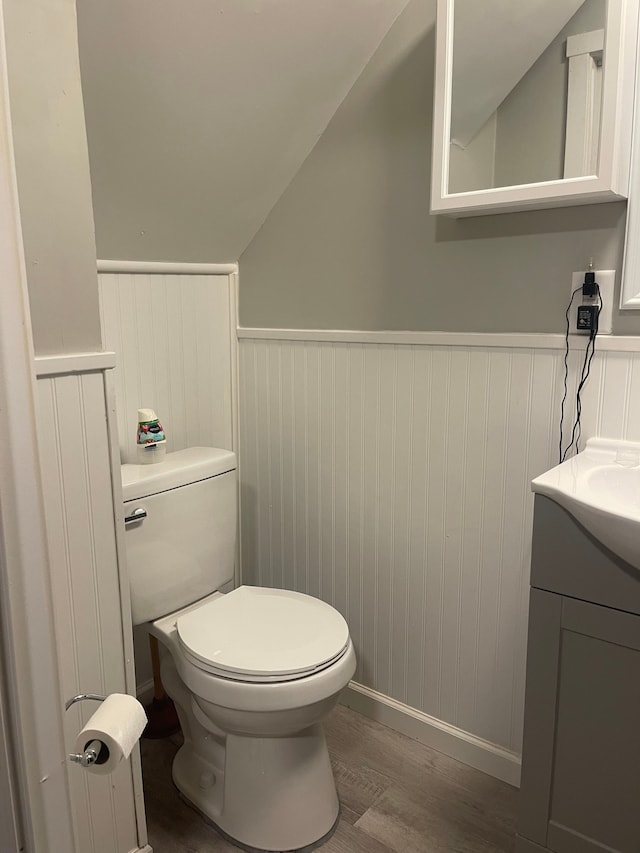 bathroom with toilet, wood-type flooring, lofted ceiling, and vanity