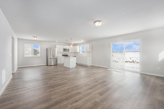 unfurnished living room with light wood-type flooring, baseboards, and a wealth of natural light