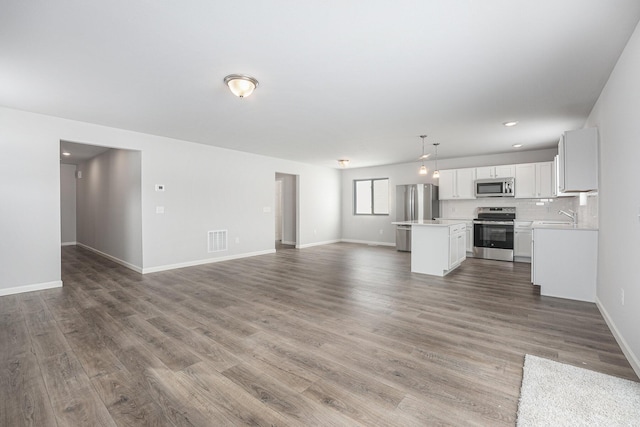 unfurnished living room featuring light wood finished floors, baseboards, visible vents, and a sink