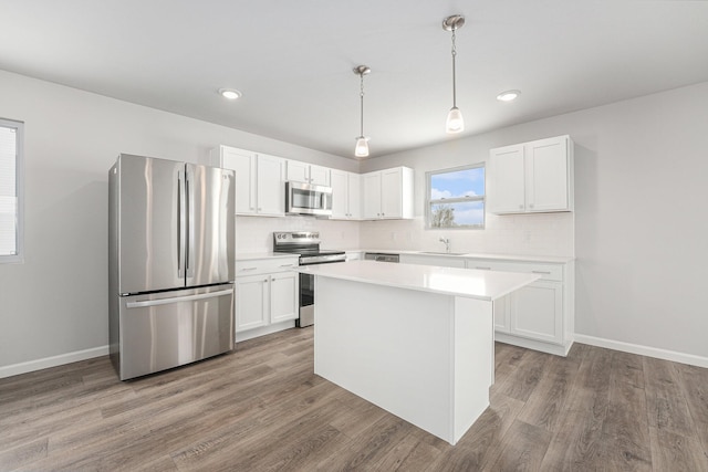 kitchen featuring wood finished floors, a sink, white cabinets, light countertops, and appliances with stainless steel finishes