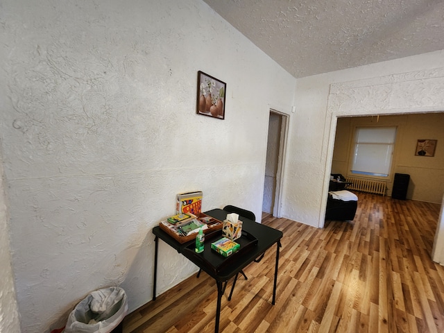 corridor with radiator heating unit, wood-type flooring, and a textured ceiling