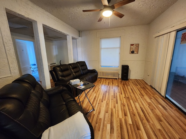 living room with a textured ceiling, light wood-type flooring, radiator, and ceiling fan