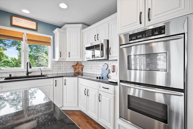 kitchen with appliances with stainless steel finishes, backsplash, sink, dark stone countertops, and white cabinetry