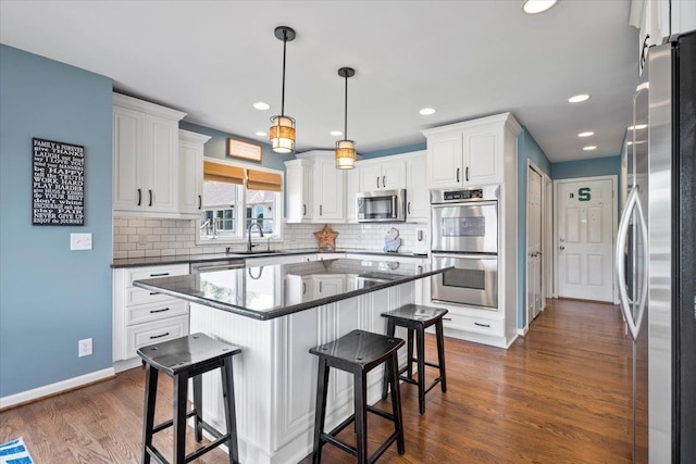 kitchen featuring appliances with stainless steel finishes, a breakfast bar, a kitchen island, dark wood-type flooring, and white cabinetry