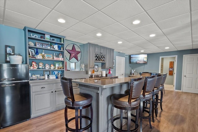 kitchen with a breakfast bar, black refrigerator, a center island, and light hardwood / wood-style floors