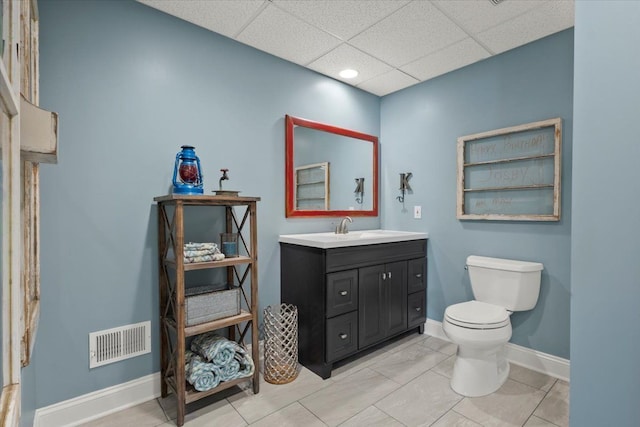 bathroom with a paneled ceiling, tile patterned flooring, vanity, and toilet