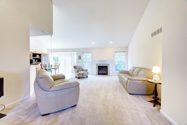 living room with light colored carpet, high vaulted ceiling, a healthy amount of sunlight, and a tiled fireplace