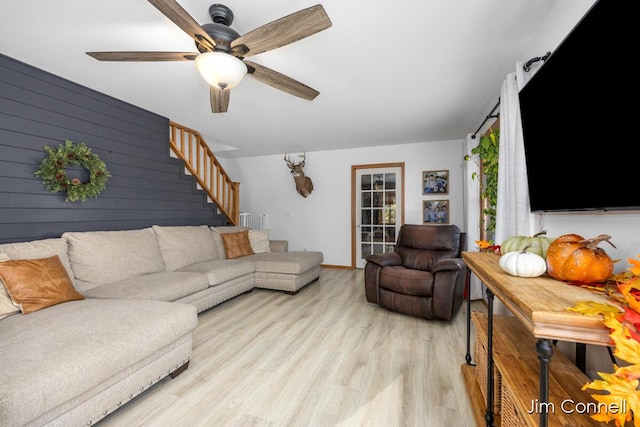 living room with wood walls, ceiling fan, and light wood-type flooring