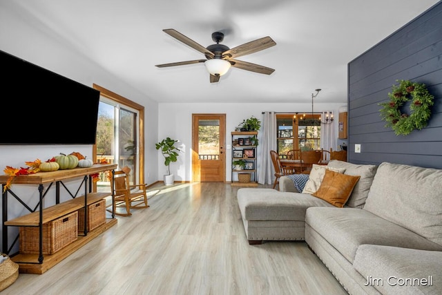 living room featuring wooden walls, ceiling fan with notable chandelier, and light hardwood / wood-style flooring