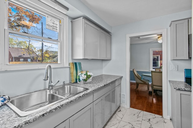 kitchen featuring light stone counters, ceiling fan, gray cabinetry, and sink