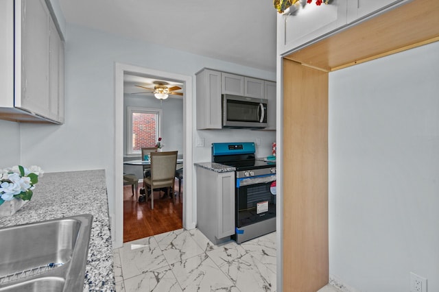 kitchen featuring gray cabinetry, light stone countertops, ceiling fan, stainless steel appliances, and light wood-type flooring