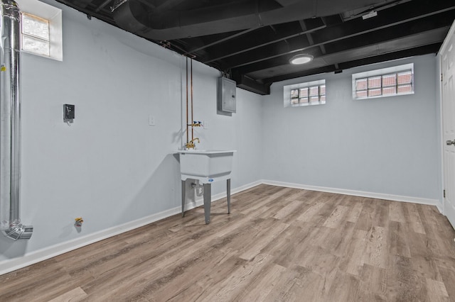 basement featuring electric panel and light hardwood / wood-style flooring