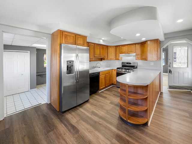 kitchen with sink, stainless steel appliances, a baseboard radiator, kitchen peninsula, and hardwood / wood-style floors