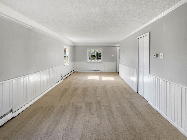 carpeted spare room featuring a textured ceiling, crown molding, and a baseboard heating unit