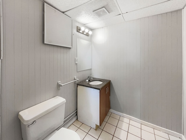 bathroom with vanity, wood walls, a drop ceiling, tile patterned flooring, and toilet